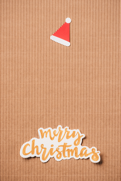 top view of santa hat and merry christmas lettering on surface - Фото, изображение