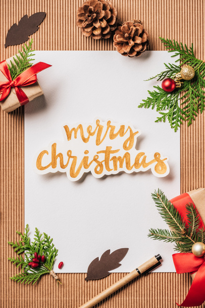 üres papír, örökzöld kúpok, díszített díszdobozok és boldog karácsonyt felületen betűkkel felülnézet - Fotó, kép