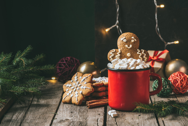 gingerbread man in cup of cocoa with marshmallows on wooden table with christmas light garland - Photo, Image