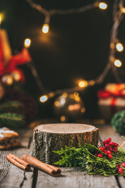 wooden stump with cinnamon sticks, fir tree and christmas light garland  - Foto, Imagen