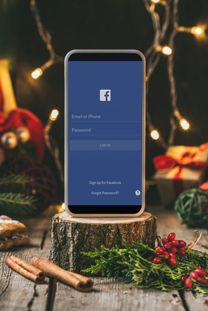 smartphone with facebook app on wooden stump with christmas decoration - Фото, зображення