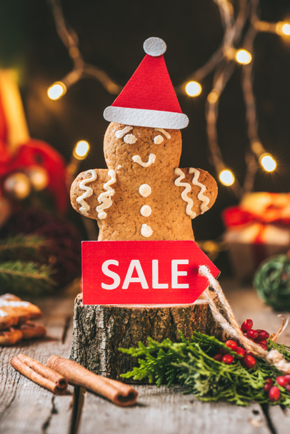 christmas gingerbread man in santa hat with red sale tag on wooden stump - Photo, Image
