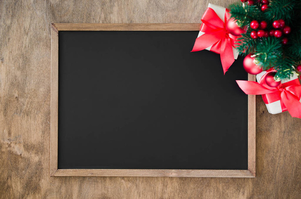 Empty blackboard with christmas decoration, red gift box, fir branches. Chalk board and Christmas trinkets. Xmas background with copy space for inscription, top view. - Photo, Image