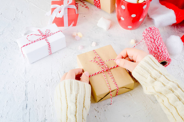 child is holding  Christmas gift box tied with a red ribbon, red cup cocoa with  marshmallow  on the white background. Christmas card Holiday Concept, copy space - Φωτογραφία, εικόνα