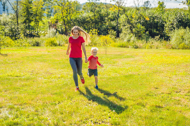 Mom and son running on green grass in park - Foto, afbeelding