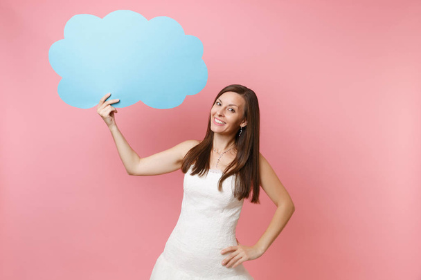 Portrait of smiling pretty bride woman in elegant white wedding dress holding blue empty blank Say cloud, speech bubble isolated on pastel pink background. Wedding celebration concept. Copy space - Photo, Image