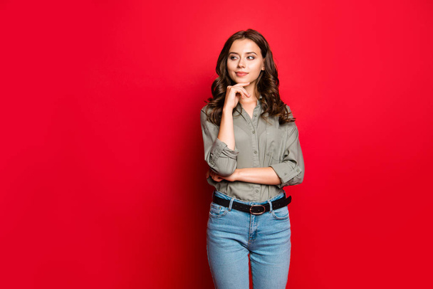 Portrait of beautiful, adorable, good-looking, curly brunette lady in blue jeans and blouse look aside isolated on bright red background with copy space for text - Foto, Imagen