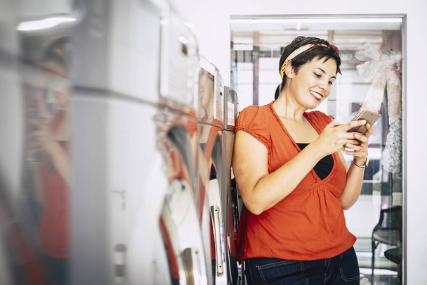 Γυναίκα με τη χρήση smartphone στο κατάστημα mat αυτόματη υπηρεσία πλυντηρίου - Φωτογραφία, εικόνα