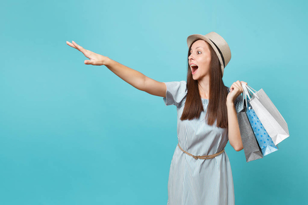 Portrait fashionable smiling beautiful caucasian woman in summer dress, straw hat holding packages bags with purchases after shopping isolated on blue pastel background. Copy space for advertisement - 写真・画像