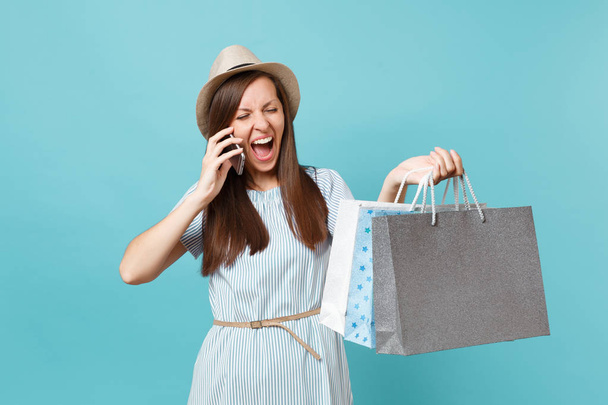 Szczęśliwa kobieta portret w Letnie sukienki, słomkowy kapelusz gospodarstwa pakiety torby z zakupami po zakupy, rozmawia Zdejmowany cellphone na białym tle na niebieskim tle pastel. Miejsce na reklamę - Zdjęcie, obraz