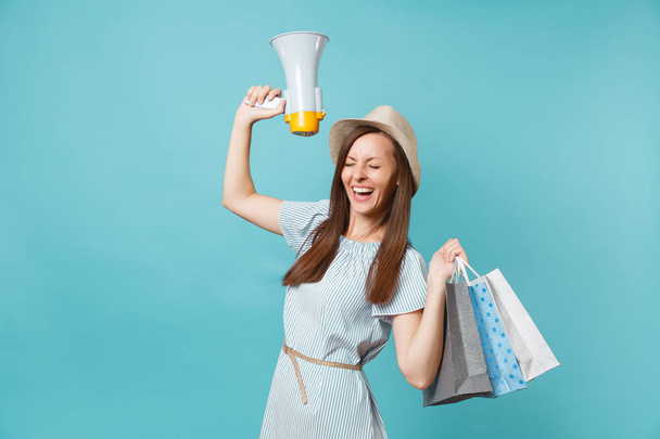 Porträt einer Frau im Sommerkleid, Hut, die nach dem Einkauf Päckchen mit Einkäufen in der Hand hält, schreit in Megafon und verkündet vereinzelt auf blauem Pastellhintergrund Rabattverkäufe. Kopierfläche für Werbung - Foto, Bild