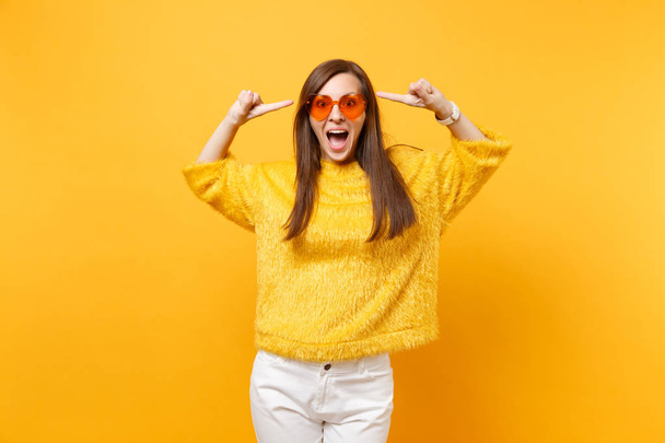 Excited happy young woman in fur sweater and heart orange glasses pointing index fingers on head isolated on bright yellow background. People sincere emotions, lifestyle concept. Advertising area - Photo, Image