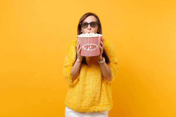 Portrét šokovaná mladá dívka v 3d brýlích imax, sledování filmu, pokrývající ústa s kýbl popcornu izolované na světle žlutém podkladu. Lidé upřímné emoce v kině, stylu života - Fotografie, Obrázek