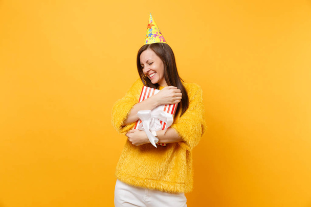 Красивая женщина в шляпе день рождения обнимая с красной коробкой с подарком, подарок празднует, наслаждаясь праздником изолированы на ярко-желтом фоне. Люди искренние эмоции, образ жизни концепции. Рекламная зона
 - Фото, изображение