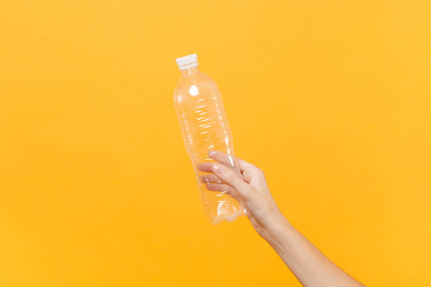 Acercamiento hembra mantenga en la mano transparente botella de plástico en blanco transparente para agua de soda aislada sobre fondo amarillo. Plantilla de embalaje maqueta. Concepto de servicio de sed. Copiar espacio. Área publicitaria
 - Foto, imagen