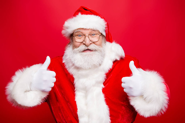 Stylish aged Santa with beard in noel costume spectacles white gloves show give thumb up demonstrate achievement advice solution isolated on bright red background make wide beaming smile look camera - Fotó, kép