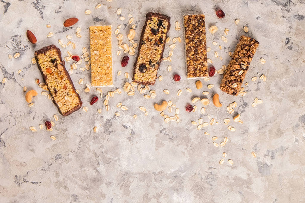 Mixed gluten free granola cereal energy bar with dried fruit & various nuts, gray concrete background. Healthy vegan super food, fitness dieting snack for sporty lifestyle. Top view, copy space. - Photo, image