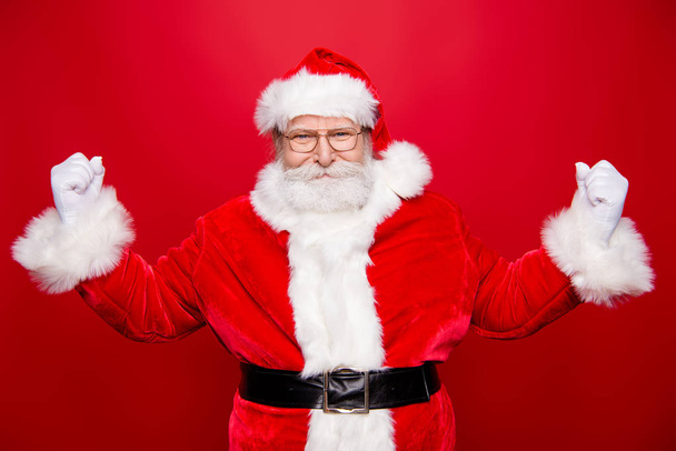 Mature serious masculine grandfather stylish Santa with white gloves beard in spectacles raised hands fists up show biceps like athlete isolated on tradition december noel eve red background - Foto, Imagen
