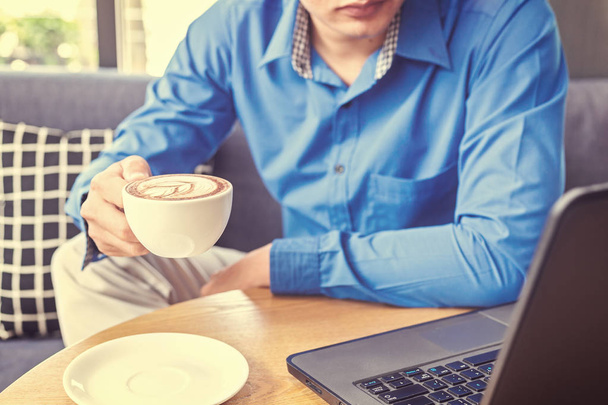 Бізнесмен тримає чашку кави. Чашка кави на столі біля ноутбука
. - Фото, зображення