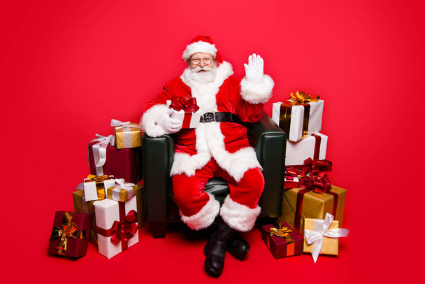 Welcome on best party! Full legs body size kind cheerful positive mature aged Santa hold small package in hand waving open palm hello hi isolated  december noel red background make big toothy smile - 写真・画像