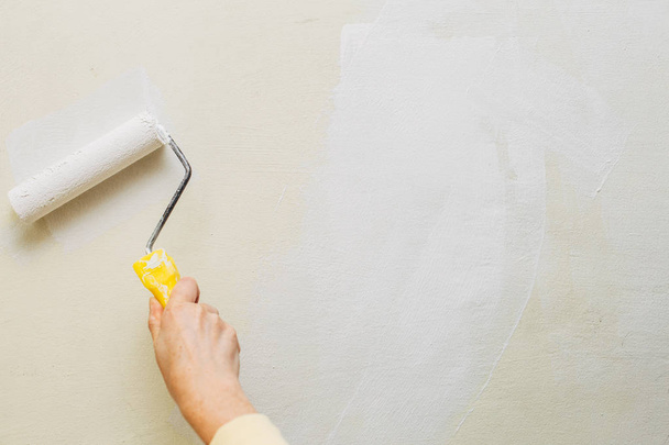 Foto van een vrouwtje schilderen een muur met een roller en witte verf. Horizontale foto. Kopiëren van ruimte - Foto, afbeelding