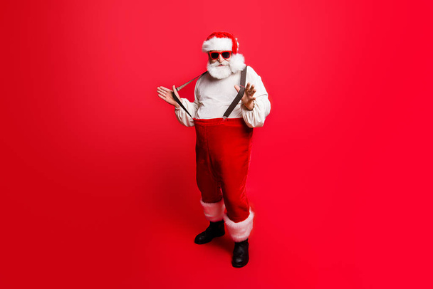 Full length body size of cheerful positive optimistic glad Santa pulling pants suspenders ready to feast festive party congrats congratulations best wishes sale discount isolated over red background - Φωτογραφία, εικόνα