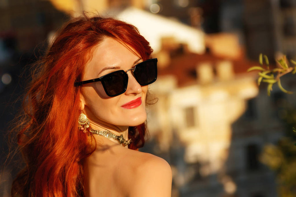 Portrait of a beautiful girl with red hair in a birch blouse on the background of the city close-up - Фото, изображение