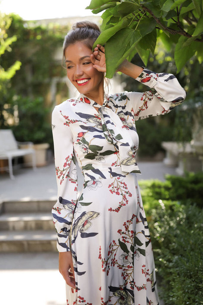Street fashion style, smiling young girl, happy, cheerful, touching the leaf, wearing colorful dress with the leaves, hair bun - Foto, imagen