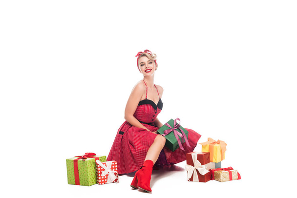 beautiful smiling woman in pin up dress sitting near pile of gift boxes isolated on white - Foto, afbeelding