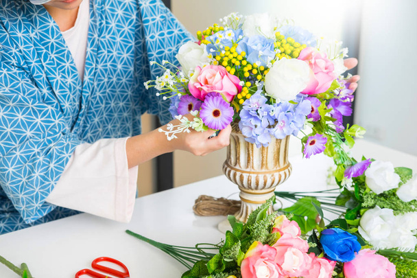 jonge vrouwen business eigenaar bloemist maken of schikken van kunstmatige bloemen vest in haar winkel, ambacht en hand maakte concept. - Foto, afbeelding