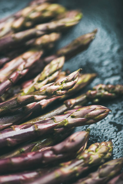 Seasonal harvest produce. Fresh raw uncooked purple asparagus over dark background - Foto, afbeelding