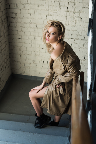 side view of stylish blond model in trench posing on stairs - Φωτογραφία, εικόνα