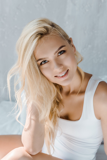portrait of beautiful young blonde woman in underwear smiling at camera in bedroom - Zdjęcie, obraz