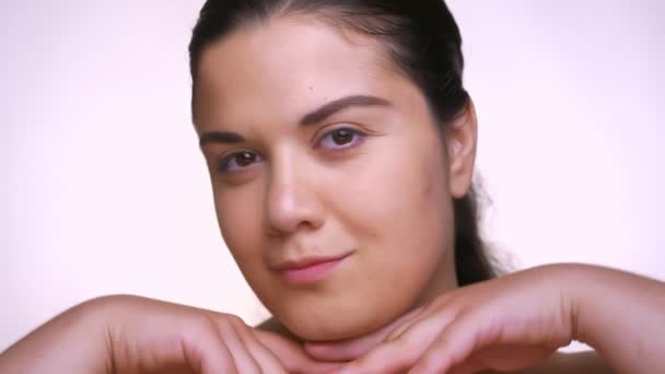 close-up face of sensitive caucasian girl touching her clear skin tenderly and looking at camera relaxed - Imágenes, Vídeo