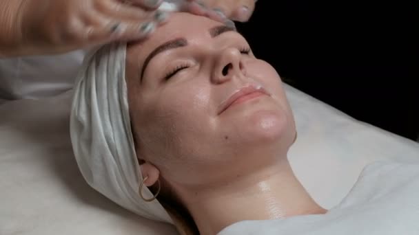 Beauty and health spa treatments. Woman on skin cleaning procedure in a beauty salon. Beautician in transparent gloves finishes soaping the face of a beautiful girl. - Footage, Video
