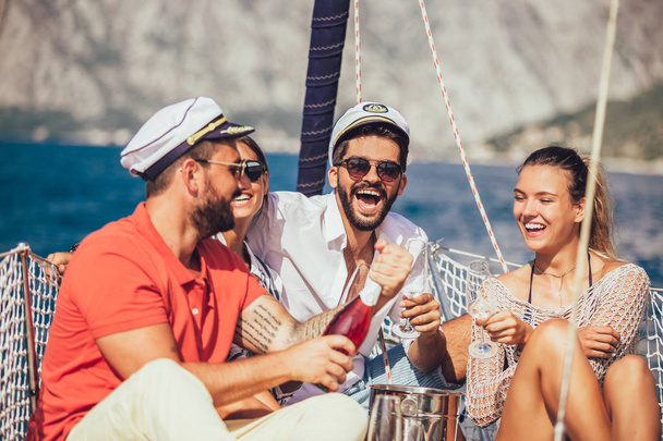 Usmívající se přátelé sedí na palubě plachetnice a baví se.Dovolená, cestování, moře, přátelství a lidé koncept - Fotografie, Obrázek