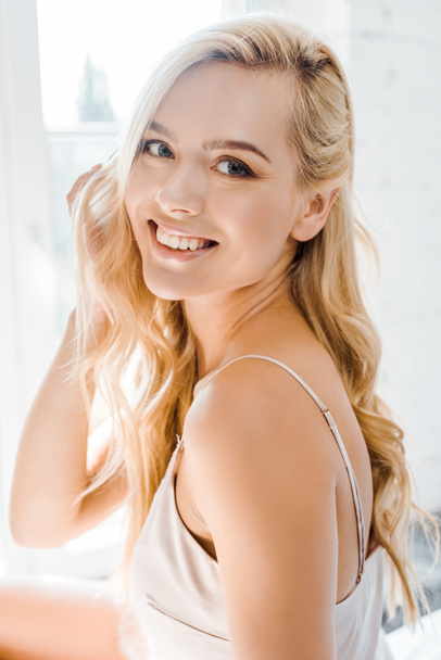 portrait of beautiful young blonde woman smiling at camera in bedroom - Fotó, kép