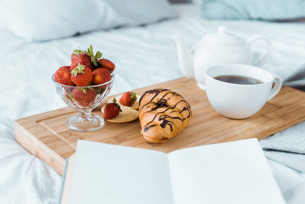 ínycsiklandozó reggelit, szamóca, croissant és kávé a fa tálcán ágyon - Fotó, kép