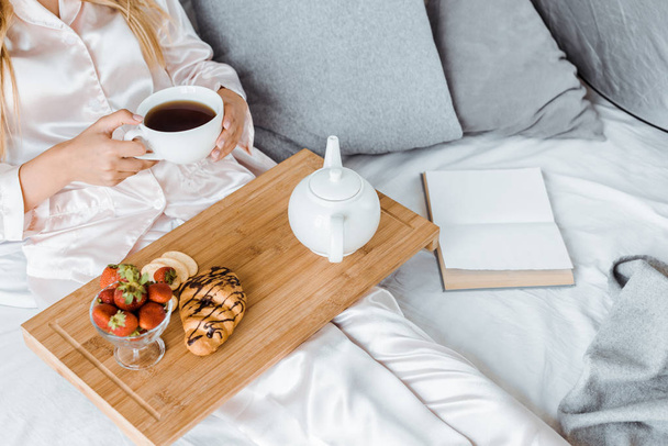 image recadrée de la femme en pyjama prenant le petit déjeuner au lit et tenant une tasse de thé
 - Photo, image