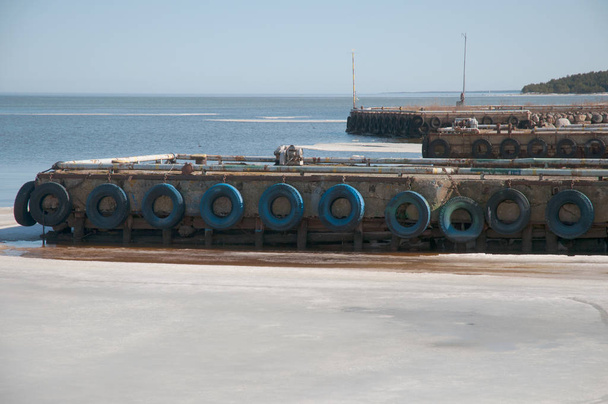 Průmyslové molo s modrým pneumatiky a bílé trubky vedle ledové vody - Fotografie, Obrázek