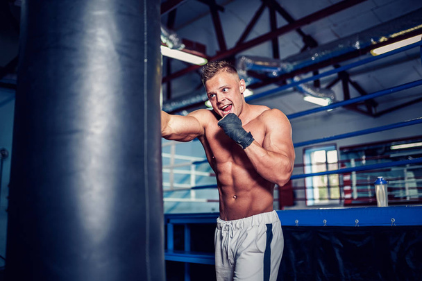 Male boxer training with punching bag in dark sports hall. - Fotografie, Obrázek