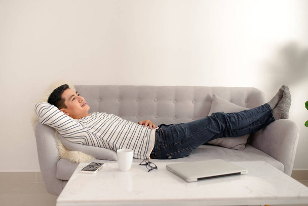 Ázsiai srác arról ábrándozik, és a többi otthon. Ázsiai férfi nyugodt, és aludni a kanapén fedett. Jóképű férfi modell. - Fotó, kép