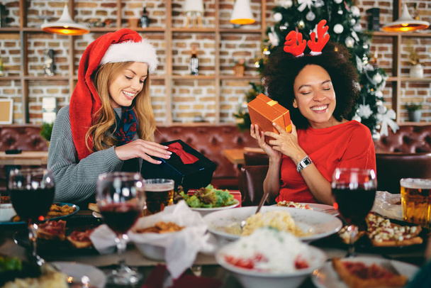 Friends opening gifts while sitting at table. Christmas holidays concept. - Fotografie, Obrázek