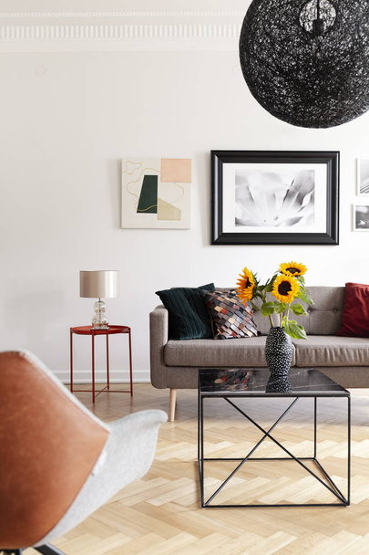 Sunflowers on table in modern living room interior with lamp and posters above sofa. Real photo - Φωτογραφία, εικόνα