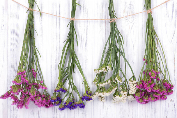  Сушеные цветы лимония разноцветные, привязанные джутовой веревкой, висят на белой деревянной стене или заборе
 - Фото, изображение