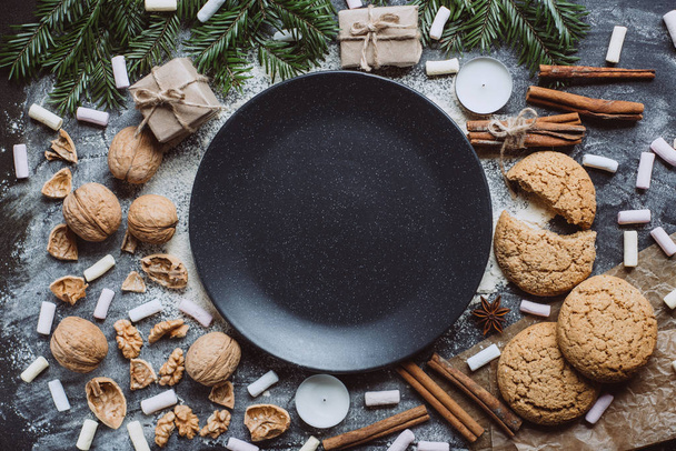 Winter background with plate, cookies, nuts, cinnamon  and marshmallow on dark background.  Flat Lay - Fotografie, Obrázek