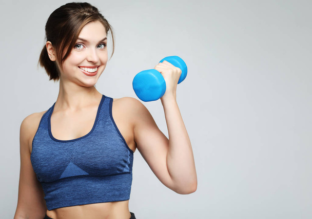 Picture of fit and healthy young woman smiling and holding dumbbelsl to shoulder. Sport and people concept. - Фото, зображення