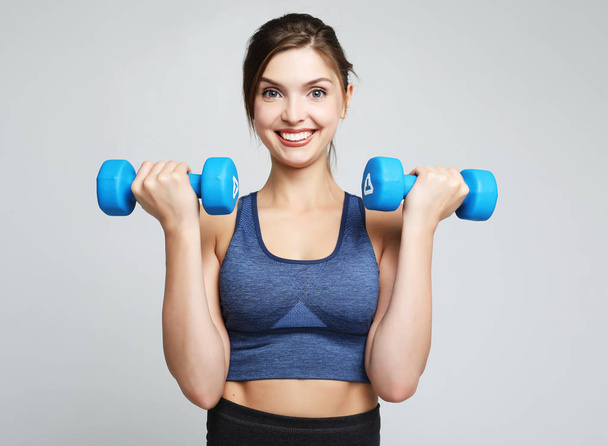 Picture of fit and healthy young woman smiling and holding dumbbelsl to shoulder. Sport and people concept. - Photo, image