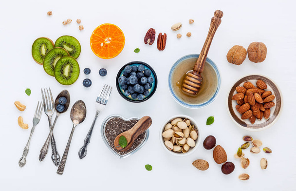 Ingredients for a healthy foods background, nuts, honey, berries, fruits, blueberry, orange, almonds, walnuts and chia seeds .The concept of healthy food set up on white wooden background. Flat lay. - Photo, Image