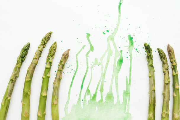 top view of fresh asparagus stems on white surface with green watercolor blots - Foto, Bild